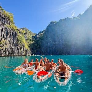 Un viaggio di gruppo WeRoad sorride per una foto in kayak trasparenti su acqua turchese accanto a scogliere rocciose.