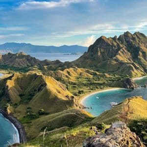 Una vista panoramica da una collina su isole verdi ondulate, baie turchesi e spiagge di sabbia bianca sotto un cielo nuvoloso.