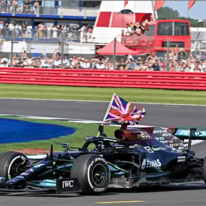 A black Formula 1 car with a British flag attached drives along a racetrack in front of a crowd of spectators in the stands.