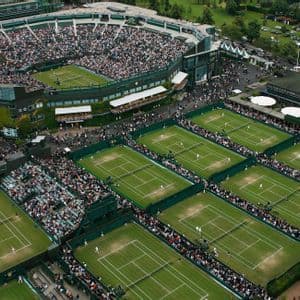 An aerial view of a large tennis stadium and multiple grass courts filled with spectators during a tournament.