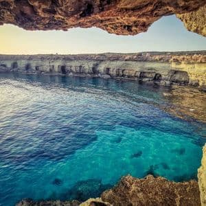 Vista dall'interno di una grotta marina su una cala con acqua turchese e scogliere rocciose.