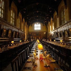 In einem großen, holzgetäfelten Speisesaal mit Porträts an den Wänden stehen lange Holztische mit Gedecken und Lampen.