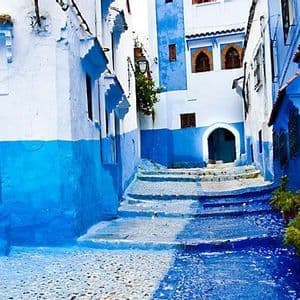 Un callejón estrecho y serpenteante de adoquines con escalones de piedra entre edificios pintados en vibrantes tonos de azul y blanco.