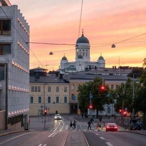 Blick auf eine Stadtstraße mit Straßenbahnschienen und einer großen weißen Kathedrale mit grünen Kuppeln, die sich vor einem Sonnenuntergangshimmel abzeichnet.