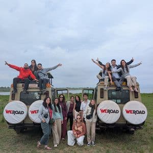 Un grupo de WeRoad posa para una foto, algunos de pie y otros sentados encima de dos vehículos de safari en un campo de hierba.