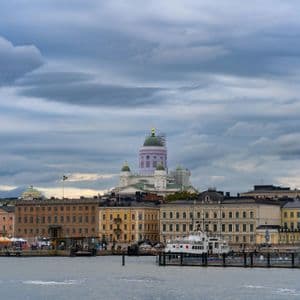 Eine Stadtsilhouette mit einem großen Dom und farbenfrohen Gebäuden, vom Wasser aus unter bewölktem Himmel gesehen.