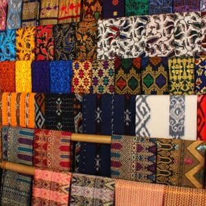 Un primo piano di tessuti colorati con vari motivi intricati, piegati ed esposti in file su aste di legno.