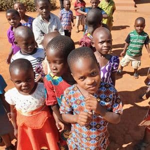 Ripresa dall'alto di un gruppo di bambini con vestiti colorati in piedi su un terreno di terra rossastra.