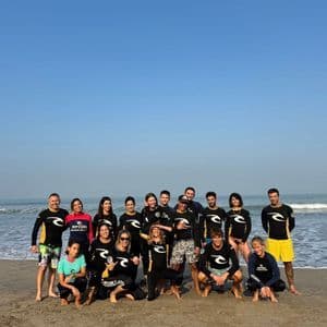 Un gruppo WeRoad in muta da sub posa per una foto su una spiaggia sabbiosa con l'oceano alle spalle.