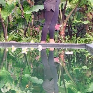 Due donne in posa yoga accanto a una piscina riflettente circondata da una lussureggiante vegetazione verde, creando un riflesso simmetrico nell'acqua.