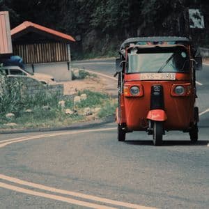 Un tuk-tuk rosso percorre una strada asfaltata e tortuosa circondata da una vegetazione lussureggiante.