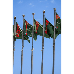 Una fila di bandiere del Turkmenistan che sventolano su aste d'argento contro un cielo azzurro chiaro.