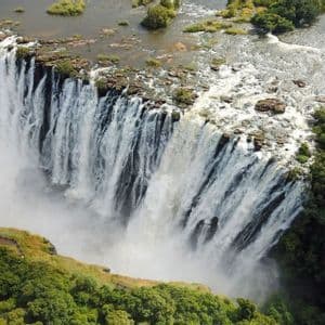 Una vista aerea di un'ampia cascata che si riversa da una scogliera rocciosa in una gola nebbiosa, circondata da alberi verdi.