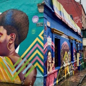 Un edificio d'angolo con murales colorati e una bandiera colombiana appesa, su una stretta strada acciottolata e bagnata.