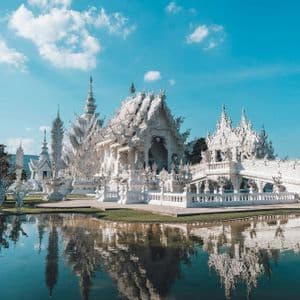 Un tempio bianco ornato con guglie intricate che si riflette in uno specchio d'acqua calmo sotto un cielo azzurro con nuvole.