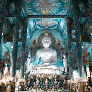 Una grande statua bianca di un Buddha seduto all'interno di un tempio con intricate decorazioni blu e oro su pareti e soffitto.