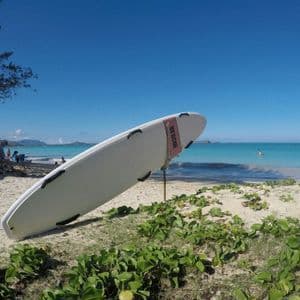 Una tavola da surf di salvataggio bianca si erge su una spiaggia sabbiosa accanto a un'acqua turchese sotto un cielo azzurro e limpido.