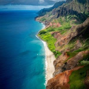 Vista aerea di una costa frastagliata e verdeggiante con una spiaggia sabbiosa che incontra l'oceano turchese sotto un cielo nuvoloso.