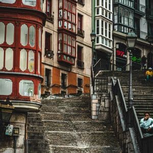 Un ripido sentiero di ciottoli e una scala in pietra parallela che sale tra gli edifici con balconi chiusi e colorati.