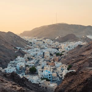 A town of white buildings nestled in a rocky valley surrounded by mountains under a hazy golden sky.