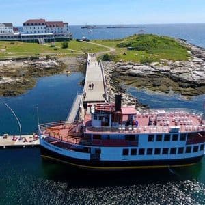 Una vista aerea di una grande barca da turismo attraccata a un lungo molo collegato a un'isola erbosa con diversi edifici bianchi.
