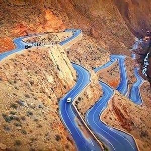 Veduta aerea di una strada tortuosa con numerosi tornanti che scende attraverso un ripido canyon roccioso di colore rosso.