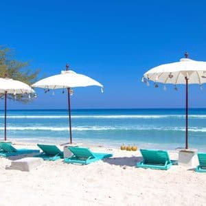 Türkisfarbene Liegestühle und weiße Sonnenschirme stehen an einem weißen Sandstrand mit Blick auf das türkisfarbene Meer unter einem klaren blauen Himmel.