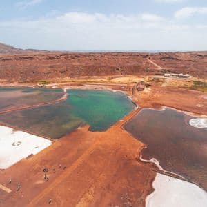 Une vue aérienne d'un voyage de groupe WeRoad marchant sur de la terre rouge le long de marais salants multicolores avec la mer en arrière-plan.