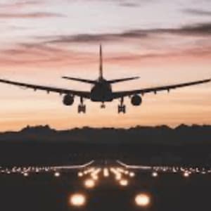An airplane seen from behind as it prepares to land on an illuminated runway at sunset.