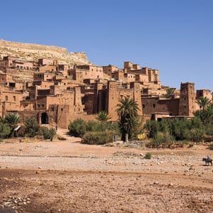 Un tradizionale villaggio di mattoni di fango, arroccato su una collina, con una persona che attraversa un letto di fiume asciutto a dorso d'asino.
