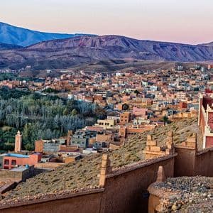 Panorama di una città con edifici in terracotta incastonata in una valle, con aspre montagne che si ergono sullo sfondo al crepuscolo.