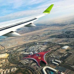 Eine Luftaufnahme aus einem Flugzeug, die seine Tragfläche über einer ausgedehnten Stadtlandschaft mit einem großen, roten, sternförmigen Gebäude zeigt.