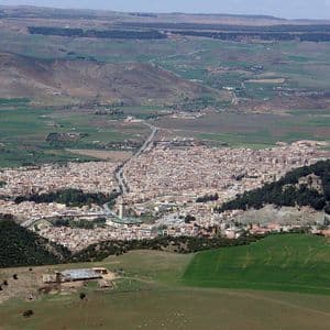Una veduta aerea di una città tentacolare situata in una valle, circondata da dolci colline verdi e marroni e foreste.
