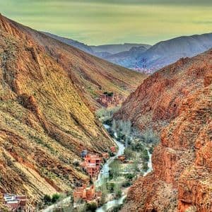 Una vista su un canyon profondo e roccioso, dove una strada e un fiume si snodano tra piccoli villaggi con edifici rosso mattone.