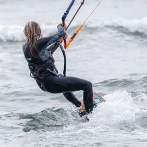 Una persona in muta nera, vista da dietro, che fa kitesurf su acqua mossa con onde.