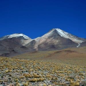 Due grandi montagne innevate dominano un vasto altopiano arido, con erba secca, sotto un cielo azzurro e limpido.