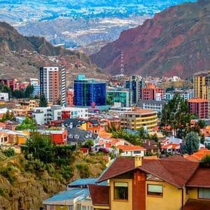 Un paesaggio urbano vivace con un mix di grattacieli e case, incastonato in una valle tra aspre montagne bruno-rossastre.