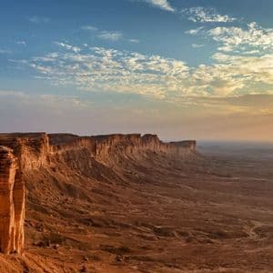 Un viaggio di gruppo WeRoad cammina lungo il bordo di una vasta scarpata rocciosa al tramonto, con vista su uno sconfinato paesaggio desertico.