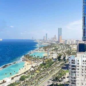 Una vista aerea del litorale di una città moderna con grattacieli, palme e spiagge con acqua turchese accanto a un mare blu profondo.