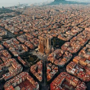 An aerial view of a large, ornate cathedral at the center of a dense city with a grid layout during sunset.