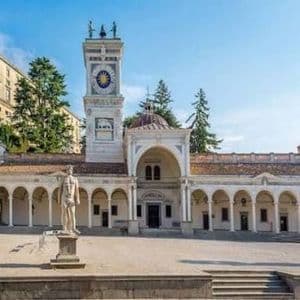 Un edificio storico bianco con una loggia ad archi e una torre dell'orologio in una piazza soleggiata con statue.