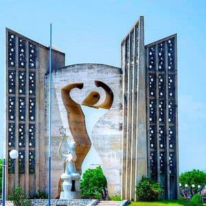 Un monumento moderno in cemento che presenta una grande figura astratta e una statua più piccola che tiene una stella, situato in un parco verde.