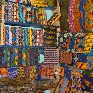 Una vasta varietà di tessuti africani wax colorati e fantasia, impilati ed esposti su scaffali di legno in una bancarella del mercato.