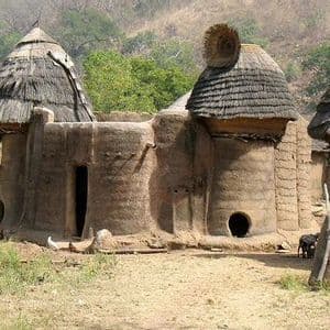 Capanne di fango rotonde e tradizionali con tetti conici di paglia in un villaggio rurale ai piedi di una collina.