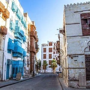 Una strada stretta e vuota affiancata da edifici storici con muri imbiancati a calce e balconi in legno intagliati blu e marroni.