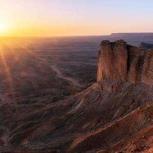 Il sole al tramonto tinge d'oro un vasto canyon desertico con ripide scogliere rocciose.
