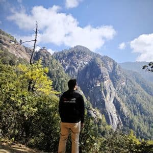 Un Group Leader WeRoad visto di spalle, che ammira un monastero incastonato in una scogliera su una montagna boscosa.