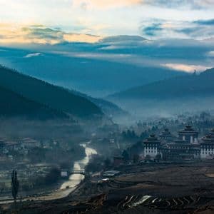 Eine Stadt mit traditioneller Architektur liegt in einem nebligen Tal zwischen Bergen, einem Fluss und terrassierten Feldern.
