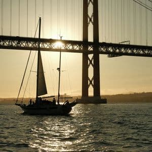 Un viaggio di gruppo WeRoad su una barca a vela stagliata contro il tramonto mentre naviga sotto un grande ponte sospeso.