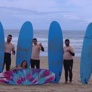 Un gruppo di viaggio WeRoad sorride e posa con le proprie tavole da surf su una spiaggia sabbiosa di fronte all'oceano.